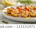 Grilled shrimp with lemon and fresh herbs on white plate, with a sprinkle of spices creating an elegant presentation 113131971