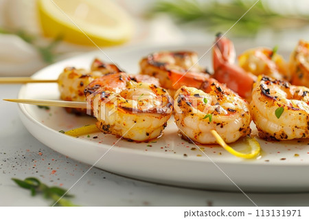 Grilled shrimp with lemon and fresh herbs on white plate, with a sprinkle of spices creating an elegant presentation 113131971