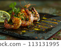 Close-up of charred shrimps with vibrant spices on a black slate, garnished with fresh herbs and lemon. 113131995