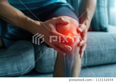 Man sitting on a couch and holding his knee. he having knee pain. Generative AI 113132034