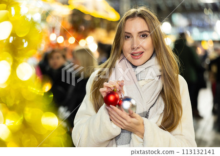 Girl with ball for Christmas tree in her hands stands in middle of New Year market 113132141