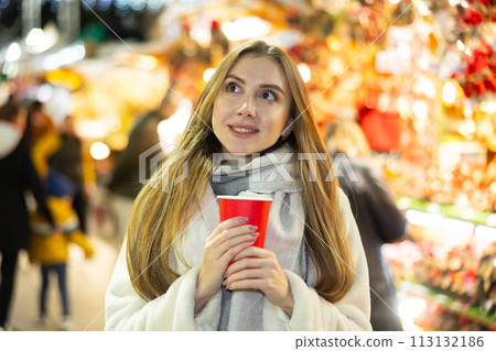 Young woman stands with glass of hot coffee in her hands and enjoys festive New Year atmosphere Young woman stands with glass of hot coffee in her hands and enjoys festive New Year atmosphere 113132186