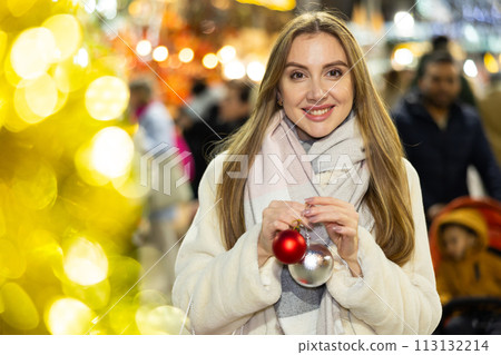 Girl with ball for Christmas tree in her hands stands in middle of New Year market 113132214