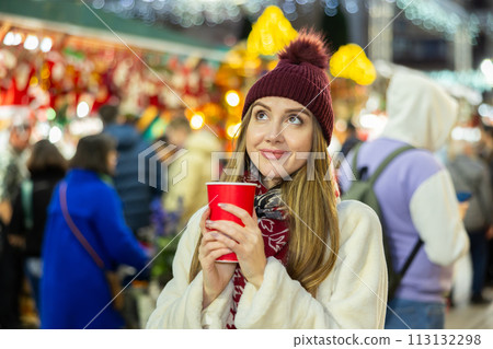 Young woman stands with glass of hot coffee in her hands and enjoys festive New Year atmosphere 113132298