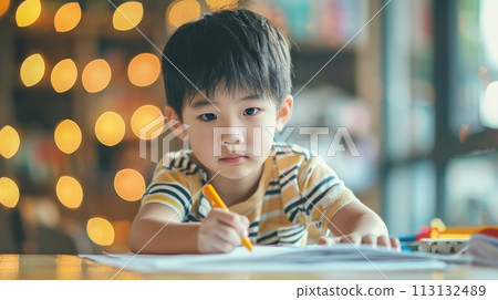 A young boy is sitting at a table with a pencil and a piece of paper A young boy is sitting at a table with a pencil and a piece of paper 113132489