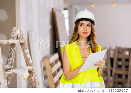 Female supervisor in safety vest and hard hat standing with papers at construction site Female supervisor in safety vest and hard hat standing with papers at construction site 113132557