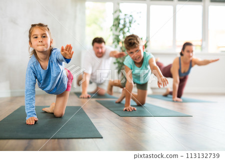 Pleasant little girl practicing table pose of yoga with her family Pleasant little girl practicing table pose of yoga with her family 113132739