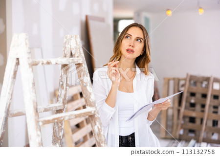 Brown-haired young woman with papers planning upcoming home overhaul Brown-haired young woman with papers planning upcoming home overhaul 113132758