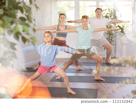 Pleasant little girl practicing warrior pose of yoga with her family Pleasant little girl practicing warrior pose of yoga with her family 113132842