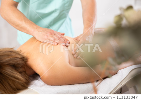 Woman dressed in tango panties receives massage of shoulder area, close-up, male masseur 113133047