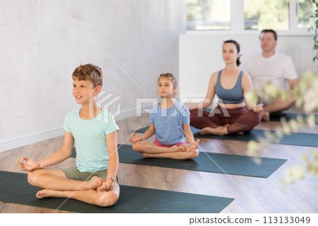 Teenage girl with her parents practices yoga in lotus position 113133049
