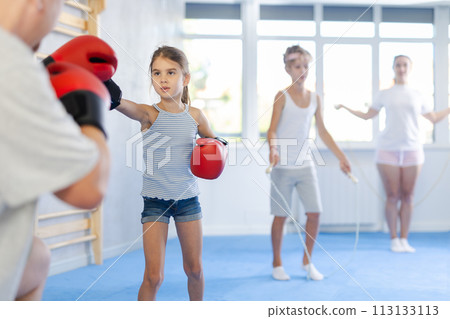 Girl and dad are boxing in gym, father helps child to work out force of blow. Girl and dad are boxing in gym, father helps child to work out force of blow. 113133113