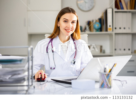 Woman doctor sitting at table and looking at camera 113133132