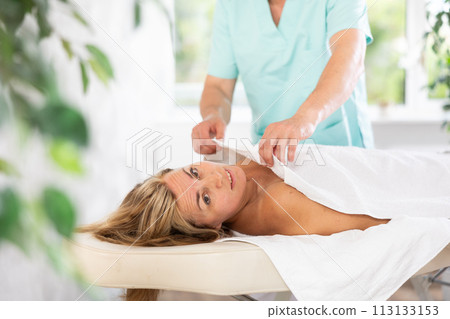 Male therapist covers woman client with white terry sheet after relaxing massage procedure 113133153