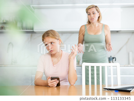 Teenage girl with smartphone making dismissive gesture to mother Teenage girl with smartphone making dismissive gesture to mother 113133345
