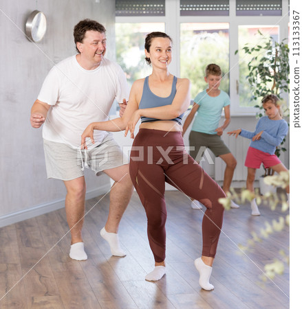 Happy middle-aged man and woman practicing dance in pairs together with their children 113133367