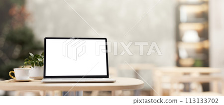 A white-screen laptop computer mockup on a wooden table in a cozy contemporary coffee shop cafe. 113133702