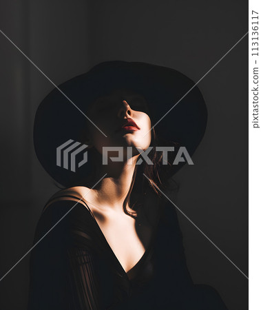A woman in a black hat is gazing upwards in the shadows 113136117