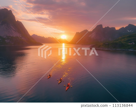 Aerial view of kayaks paddling towards the sunset in a serene coastal landscape with dramatic mountains 113136844
