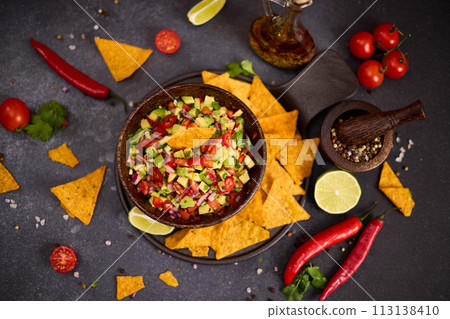 traditional salsa dip snack in wooden bowl and corn nacho chips on a table with ingredients traditional salsa dip snack in wooden bowl and corn nacho chips on a table with ingredients 113138410