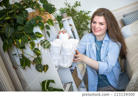 Modern housewife putting neatly folded towels, duvet covers into wicker natural eco-friendly basket Modern housewife putting neatly folded towels, duvet covers into wicker natural eco-friendly basket 113139300