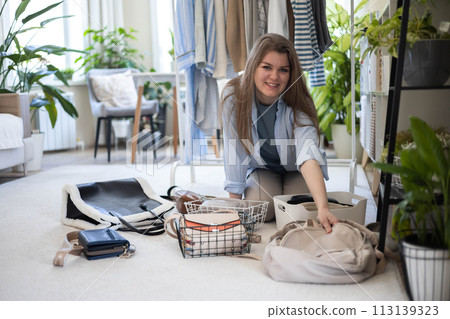 A young woman puts various women's handbags for storage in her home wardrobe. Accessories and bags. 113139323