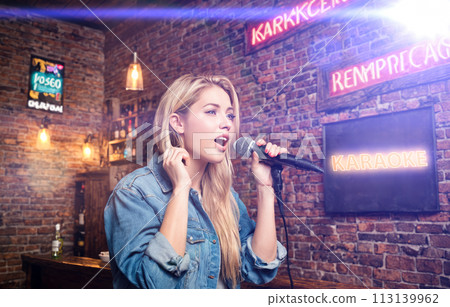 Woman singing karaoke in microphone. happy young women singing karaoke in bar. woman singing in night bar on weekend. concept with young woman in bar 113139962