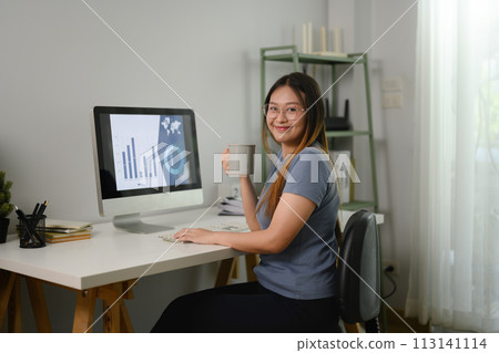 Smiling female entrepreneur drinking coffee and working at home with data and graphs 113141114