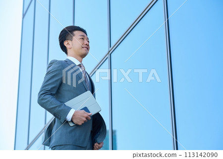 Businessman in a suit looking up at the sky outdoors Businessman in a suit looking up at the sky outdoors 113142090