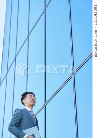 Businessman in a suit looking up at the sky outdoors Businessman in a suit looking up at the sky outdoors 113142091