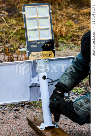 Assembly of fully autonomous, standalone LED street lighting, construction worker install support bracket to wooden pilon. 113142173