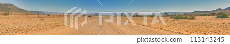 Panoramic picture over a gravel road through the desert like steppe with red sand in southern Namibia under a blue sky Panoramic picture over a gravel road through the desert like steppe with red sand in southern Namibia under a blue sky 113143245