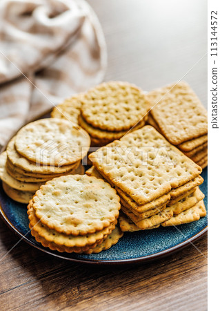A stack of crackers neatly arranged on plate on wooden tabletop. 113144572