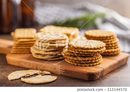 A stack of crackers neatly arranged on cutting board on wooden tabletop. 113144578
