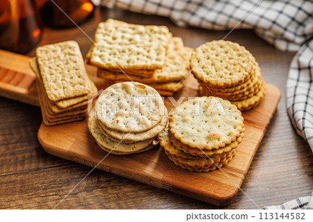 A stack of crackers neatly arranged on cutting board on wooden tabletop. 113144582
