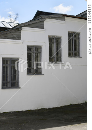 White wall of a medieval monastery building with four windows with wooden frames arranged in steps White wall of a medieval monastery building with four windows with wooden frames arranged in steps 113144583