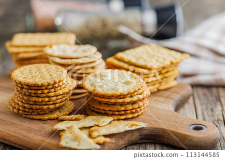 A stack of crackers neatly arranged on cutting board on wooden tabletop. 113144585