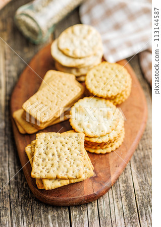 A stack of crackers neatly arranged on cutting board on wooden tabletop. A stack of crackers neatly arranged on cutting board on wooden tabletop. 113144587