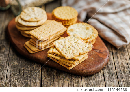 A stack of crackers neatly arranged on cutting board on wooden tabletop. A stack of crackers neatly arranged on cutting board on wooden tabletop. 113144588
