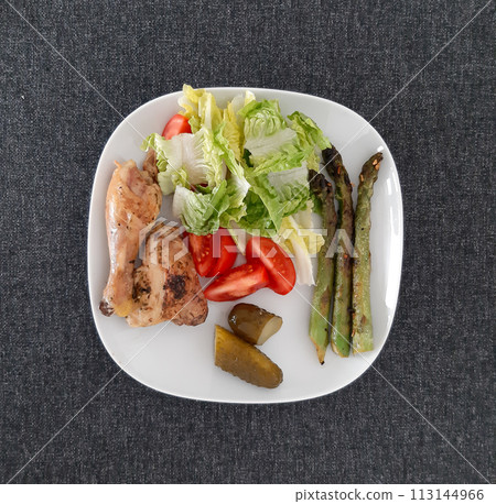 Homemade grilled chicken legs with grilled asparagus, green salad,  sliced tomato and cucumber pickles 113144966
