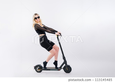 Happy young woman wear glasses riding electric scooter on background studio People lifestyle concept Happy young woman wear glasses riding electric scooter on background studio People lifestyle concept 113145485
