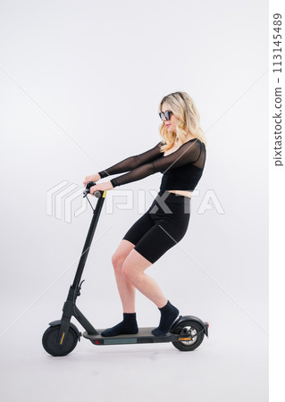 Happy young woman wear glasses riding electric scooter on background studio People lifestyle concept Happy young woman wear glasses riding electric scooter on background studio People lifestyle concept 113145489