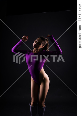 Seductive young female in violet bodysuit on dark and red background 113145596