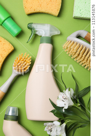 Detergents and brushes with fresh flowers on green background 113145876