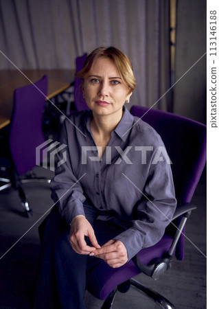 beautiful middle age business woman wearing gray shirt, wide leg pants abd black stilettos sit in purple office chair in modern workspace beautiful middle age business woman wearing gray shirt, wide leg pants abd black stilettos sit in purple office chair in modern workspace 113146188