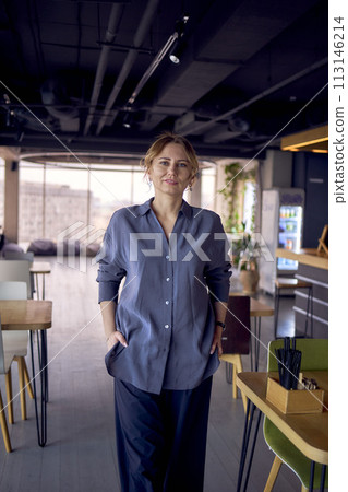 an  attractive middle age woman walks in a modern coworking neutral design, wearing wide leg pants and a silk blouse 113146214