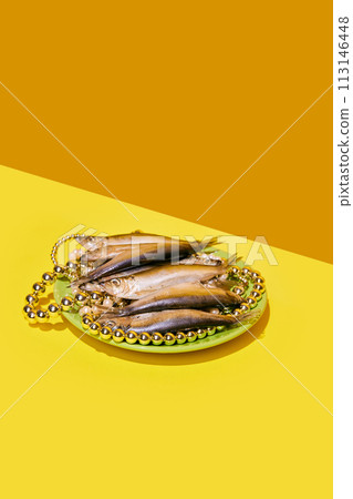 Smoked fish on a plate with pearl necklaces, on a diagonal yellow background, elegant arrangement. 113146448