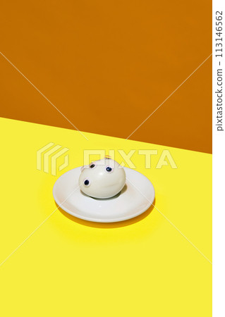 Boiled egg with googly eyes on it in small round plate lying on yellow orange background. Artistic food representation. 113146562