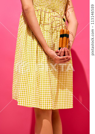 Creative image of woman hiding behind her back sausages imitating explosive item against pink background. Surrealism 113146589