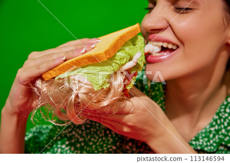 Young woman eating quirky sandwich with doll against red background. Weirdness and surrealism. Young woman eating quirky sandwich with doll against red background. Weirdness and surrealism. 113146594